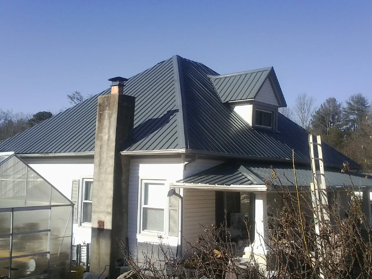 Dark blue standing seam metal roof on a white farmhouse with dormer — Slate & Tile Roof Repair by Roofing Brothers in New Bavaria