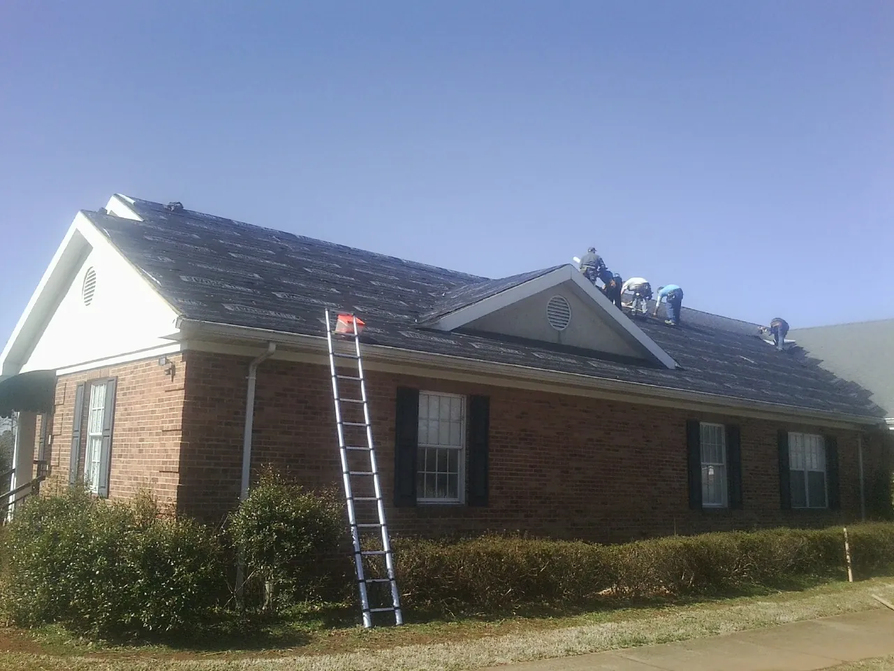 Crew tearing shingles off a brick ranch roof with a ladder set — Metal Roof Repair work by our crew in New Bavaria