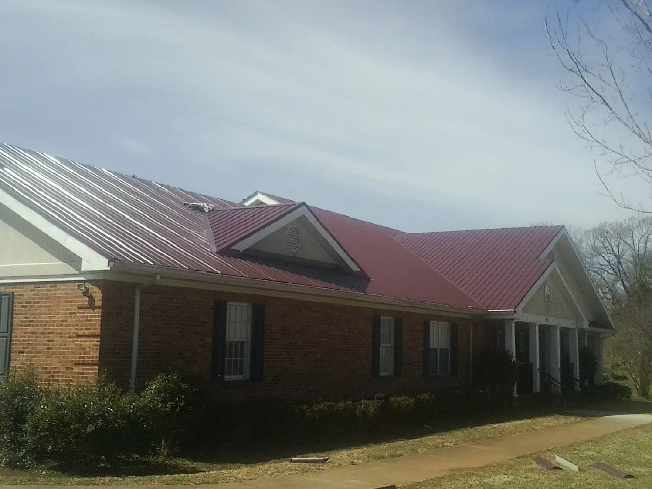 Red metal roof with gabled entries on a long brick building, from a Hail Damage Roof Repair job in New Bavaria