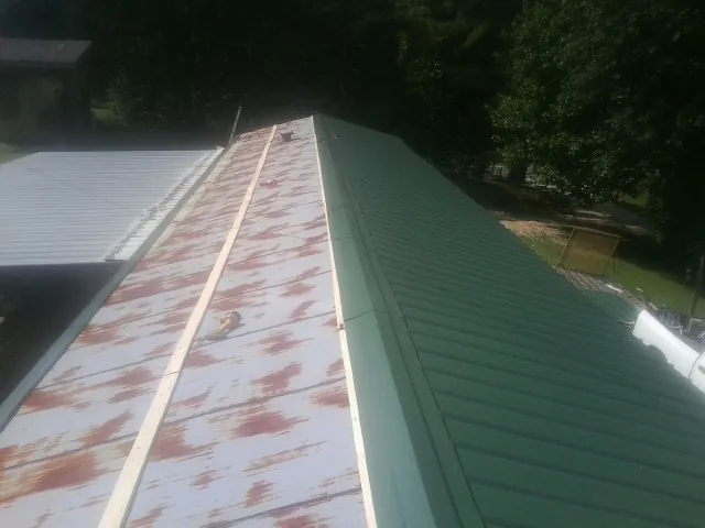 Old rusted panels beside newly installed green metal roofing — Wind Damage Roof Repair by Roofing Brothers in New Bavaria