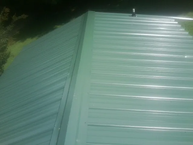 New green metal panels meeting at the ridge of a roof — Flat Roof Repair work by our crew in New Bavaria