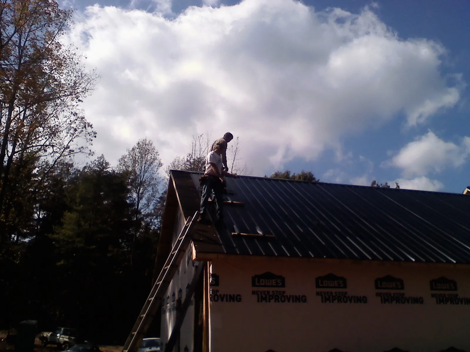 Roofer fastening dark metal panels high against a cloudy sky, from a Roof Inspection job in New Bavaria