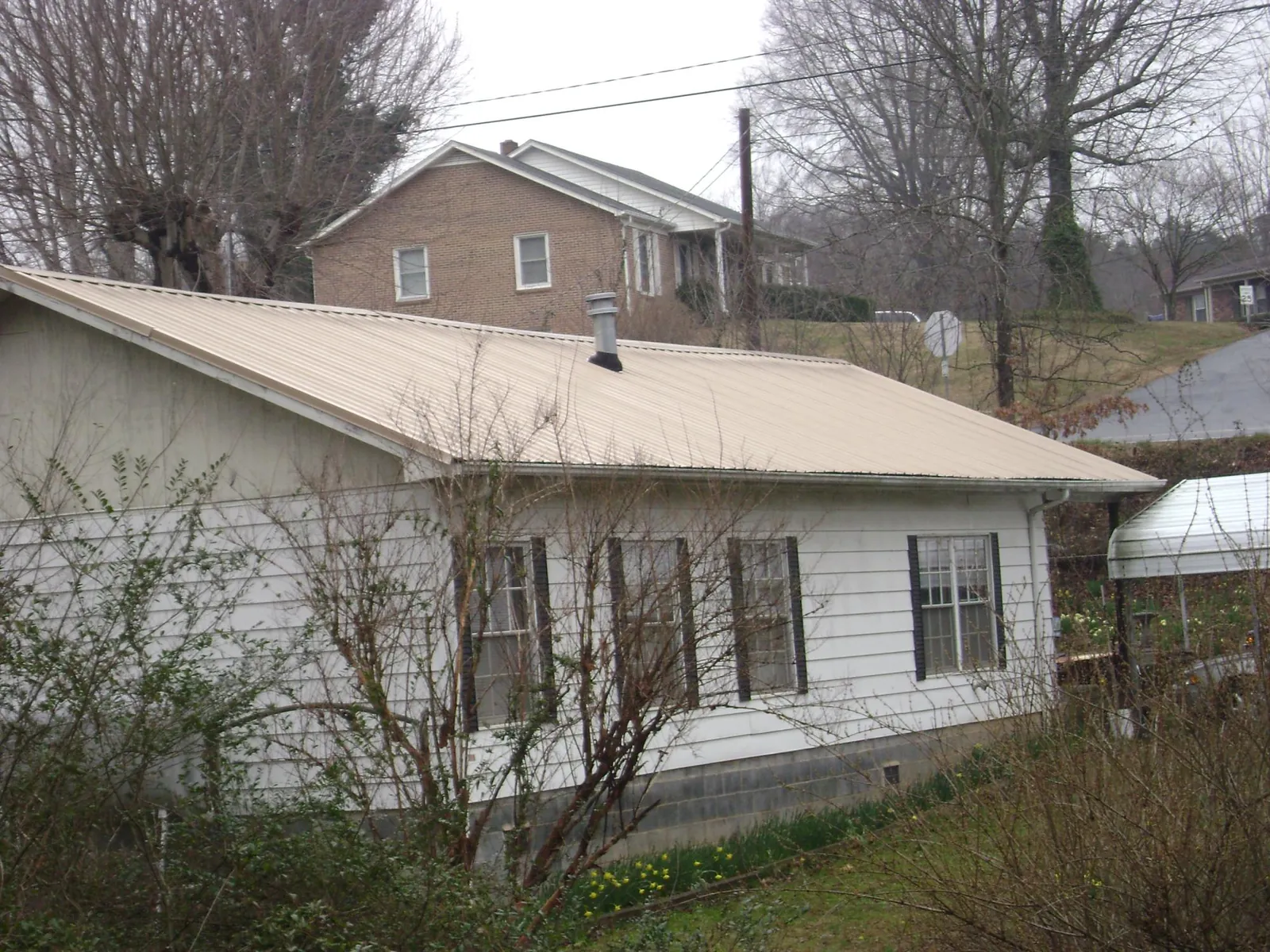 Tan metal roof on a white sided house set into a hillside — Commercial Roofing by Roofing Brothers in New Bavaria