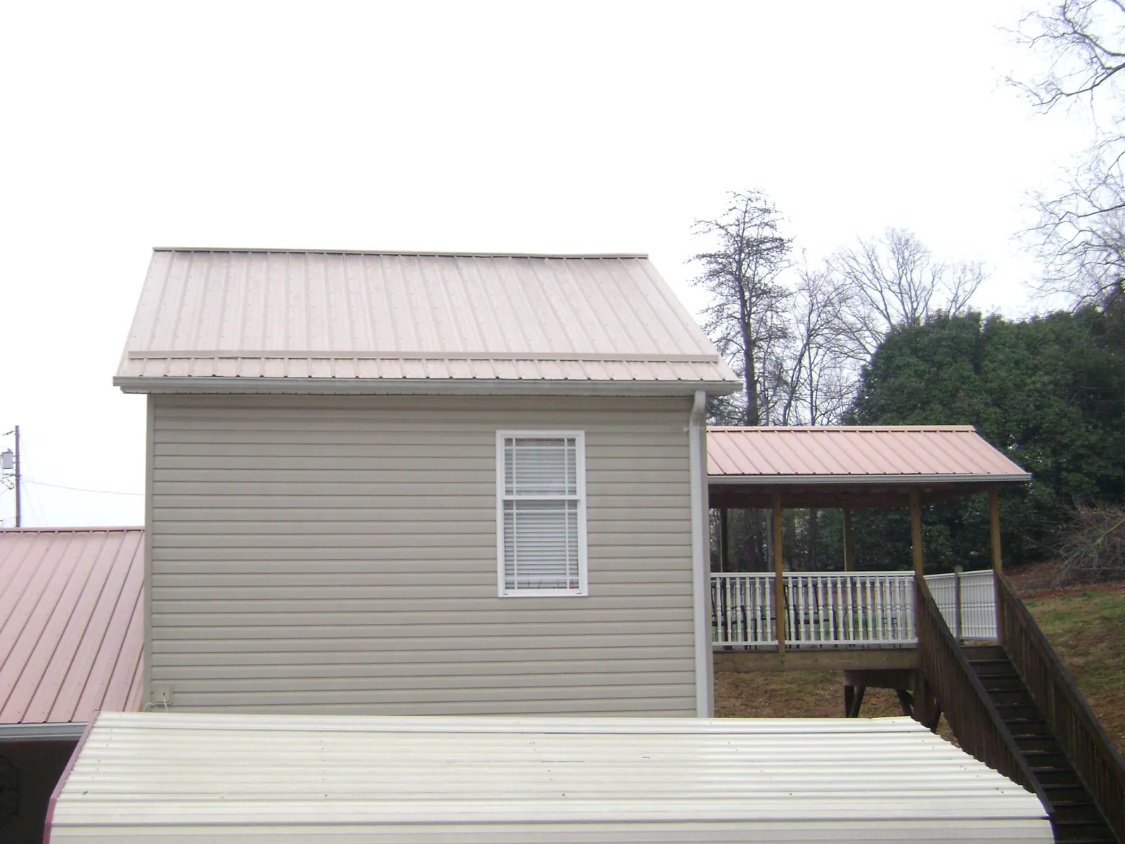 Tan metal roofs on a two story addition and attached porch, from a Roof Replacement job in New Bavaria